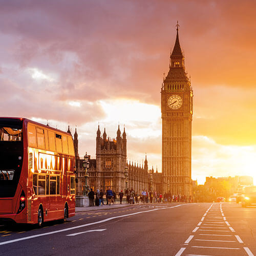 Sunset view of Big Ben and the Houses of Parliament in London, with red double-decker buses passing by