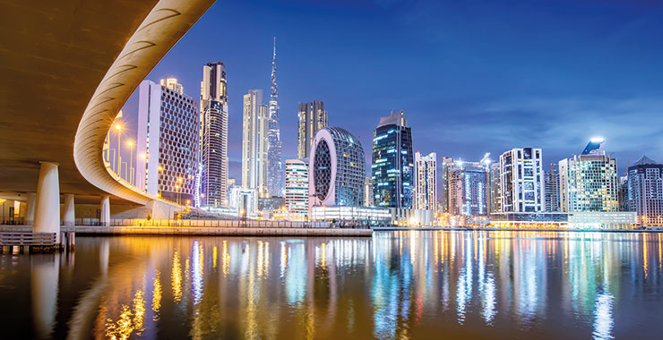 A stunning night shot of Dubai's skyline, featuring the iconic Burj Khalifa and other skyscrapers reflected in the calm waters of the Dubai Water Canal